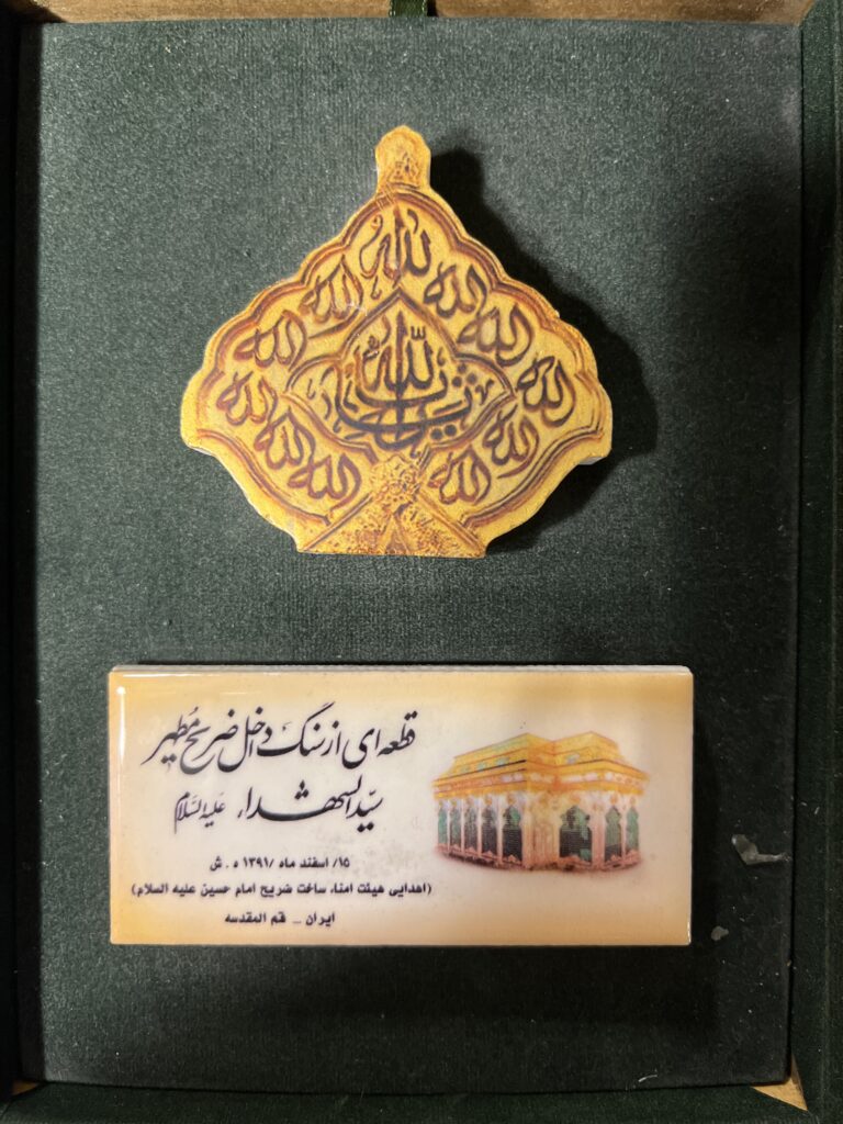 «تصویر قطعه‌ای از سنگ ضریح مطهر سیدالشهدا (ع) با نقش مذهبی، اهدایی به مناسبت مشارکت در ساخت ضریح امام حسین (ع)، نگهداری‌شده در قاب مخمل»